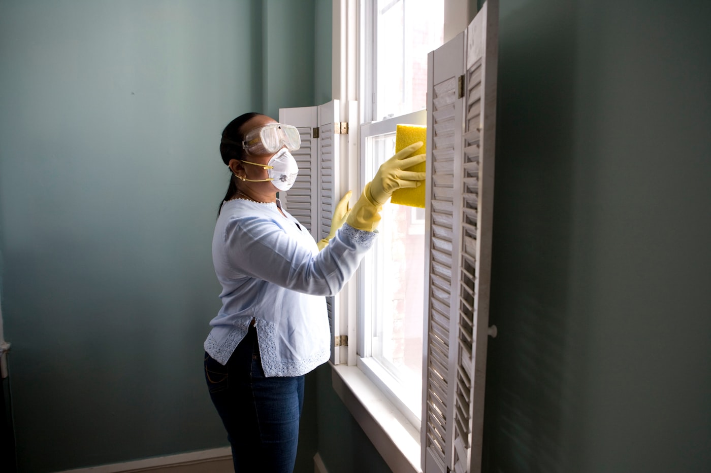 Cleaner wiping down a window in a sunlit room